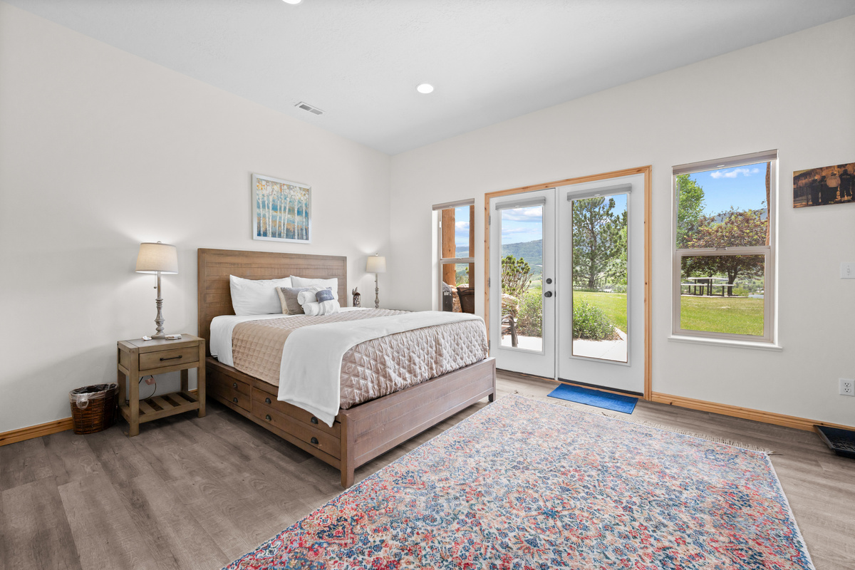 This serene bedroom features a queen-size bed, TV, and ensuite bathroom—plus direct access to a patio with a BBQ grill, seating, and stunning views.