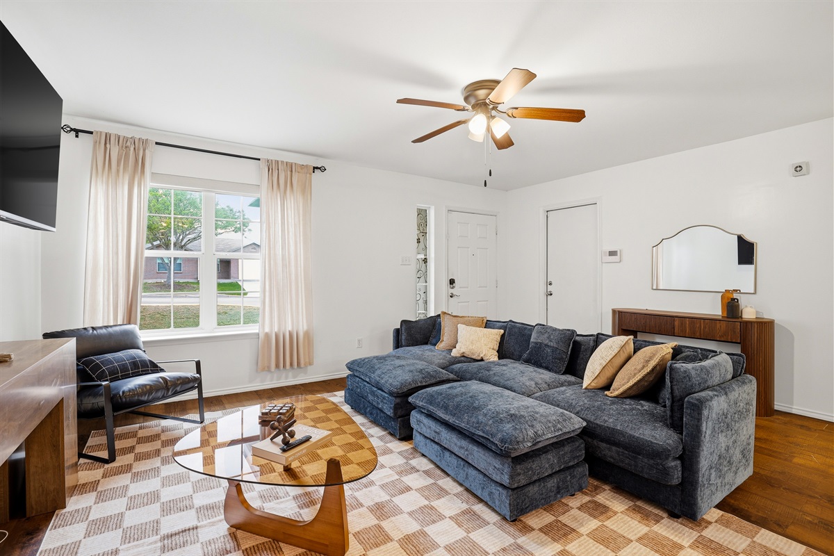 Living room with large sectional sofa, ceiling fan, and Smart TV — plenty of seating for the whole group. Open sightlines connect to the kitchen and dining area for an easy, comfortable flow.