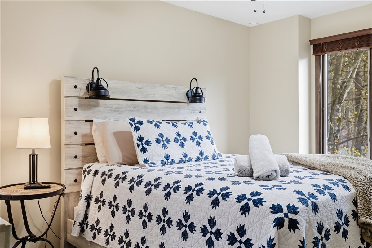 The upstairs queen bedroom features warm natural light, a dedicated workspace and a cozy cabin vibe