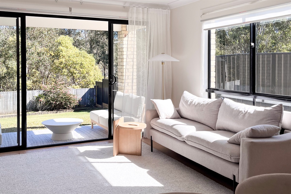 The living room has a generous sofa, bright windows and direct access to the patio and garden outlook.