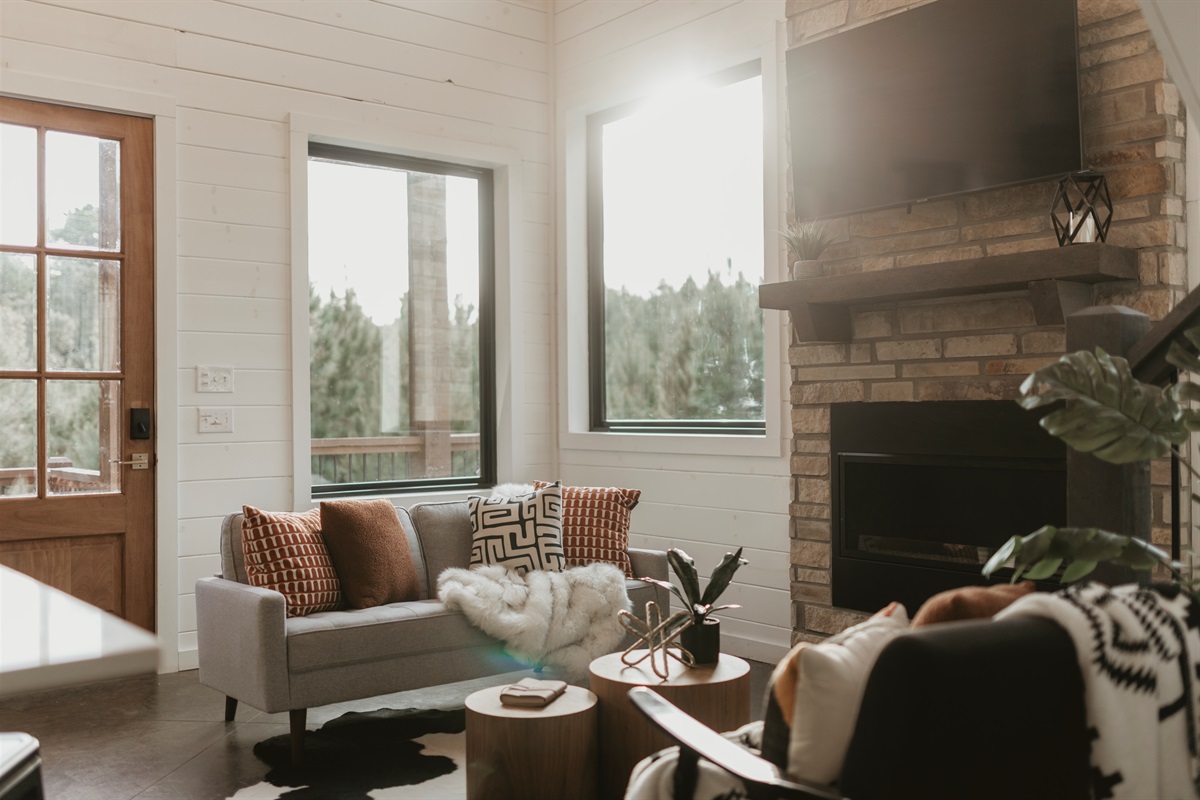 Soaring ceilings, soft sunlight, and a cozy fireplace set the tone in this warm and welcoming living room—perfect for morning coffee, game nights, or movie marathons surrounded by the pines.