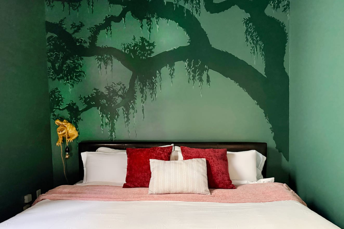 Sleep under the stars without leaving the city. The oak mural wraps around you like the bayou at midnight — moss, mystery, and a golden gator keeping watch from the bedside. Wake up when you're ready. NOLA will still be there.