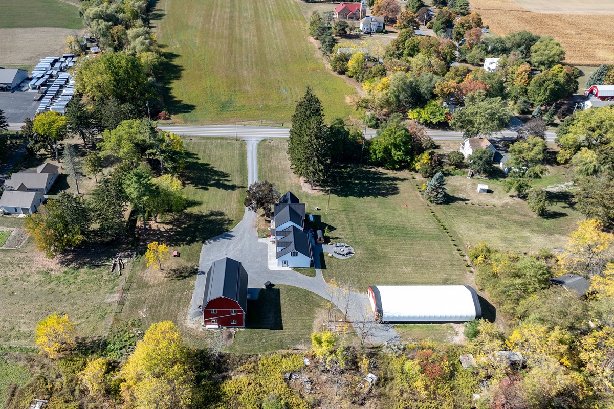 Gorgeous aerial shot highlighting the property’s large yard, barns, and scenic Finger Lakes backdrop