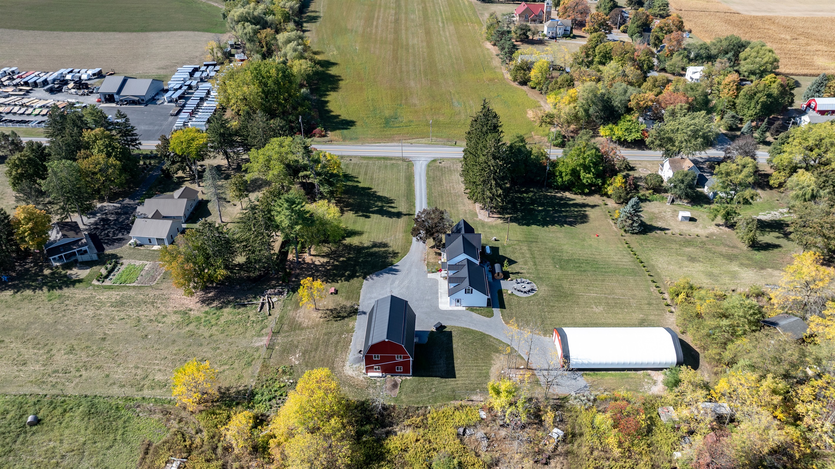 Gorgeous aerial shot highlighting the property’s large yard, barns, and scenic Finger Lakes backdrop