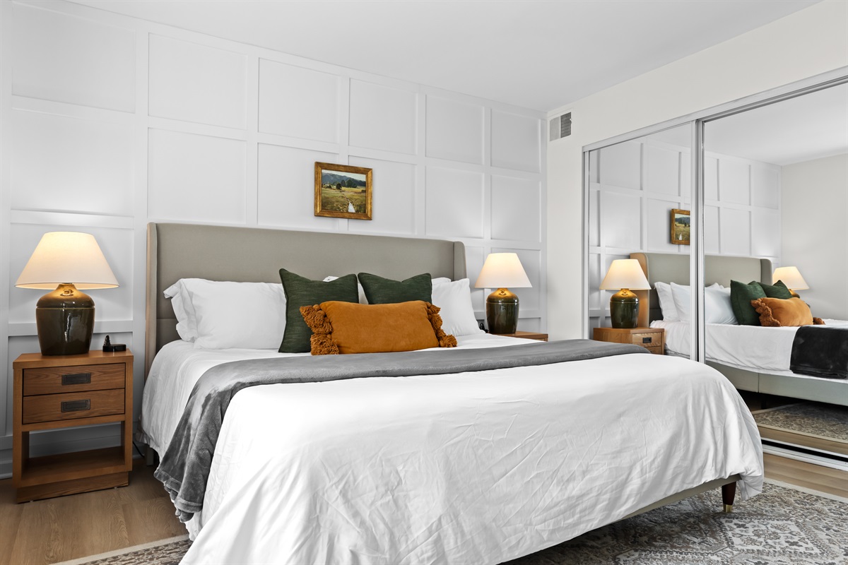 Spacious bedroom with a king bed, mirrored closet doors, and warm lighting.