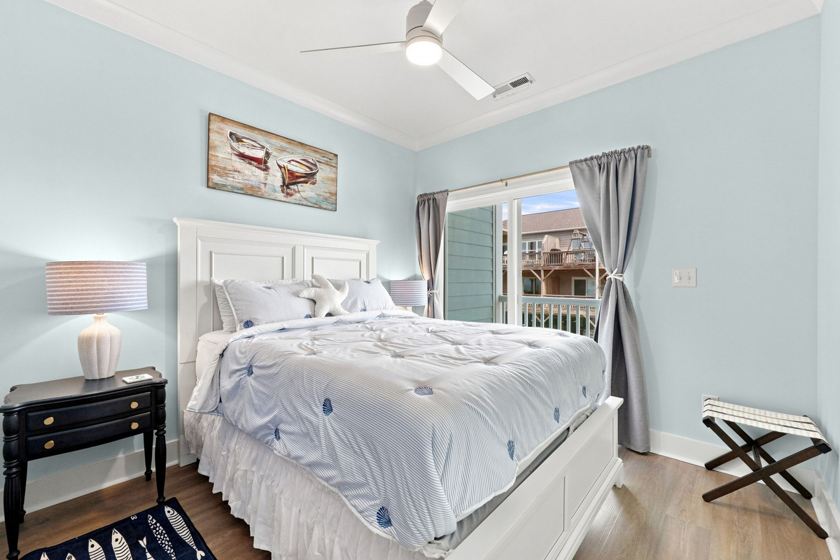 Relax in this cozy queen bedroom featuring soft coastal colors, comfortable bedding, and a private balcony door bringing in natural light