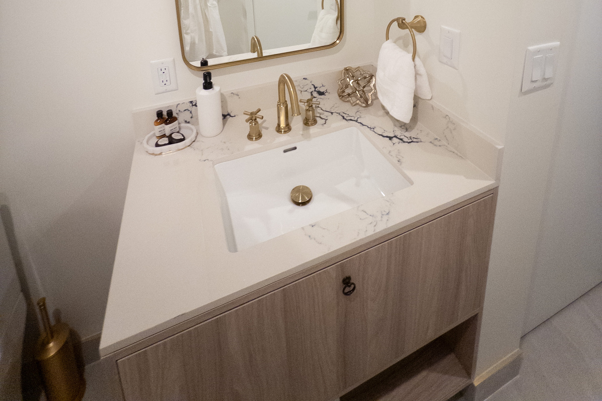 Hotel-style vanity - marble top, brushed-gold faucet and a wide backlit mirror.