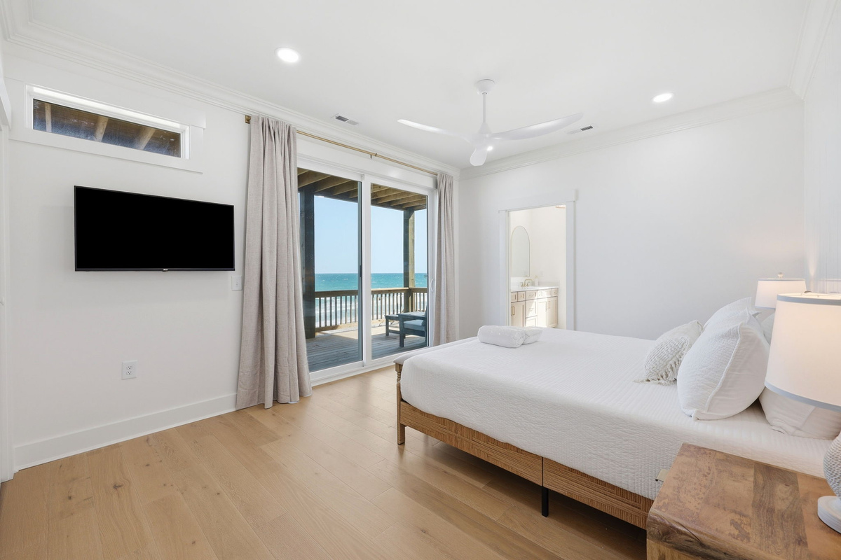 Ocean-view first-floor master bedroom with sliding glass doors to deck, TV wall, and natural wood furnishings