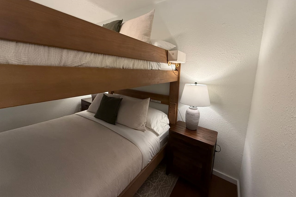 The main floor bedroom features a unique adult bunk bed with a queen-size mattress on both the top and bottom bunks, comfortably sleeping four adults. This layout is designed to maximize space without sacrificing comfort. 