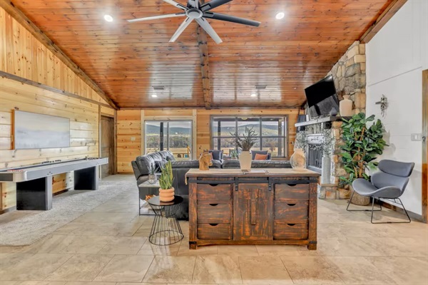 Living room with shuffleboard, stone fireplace, console stocked with games and mountain views.