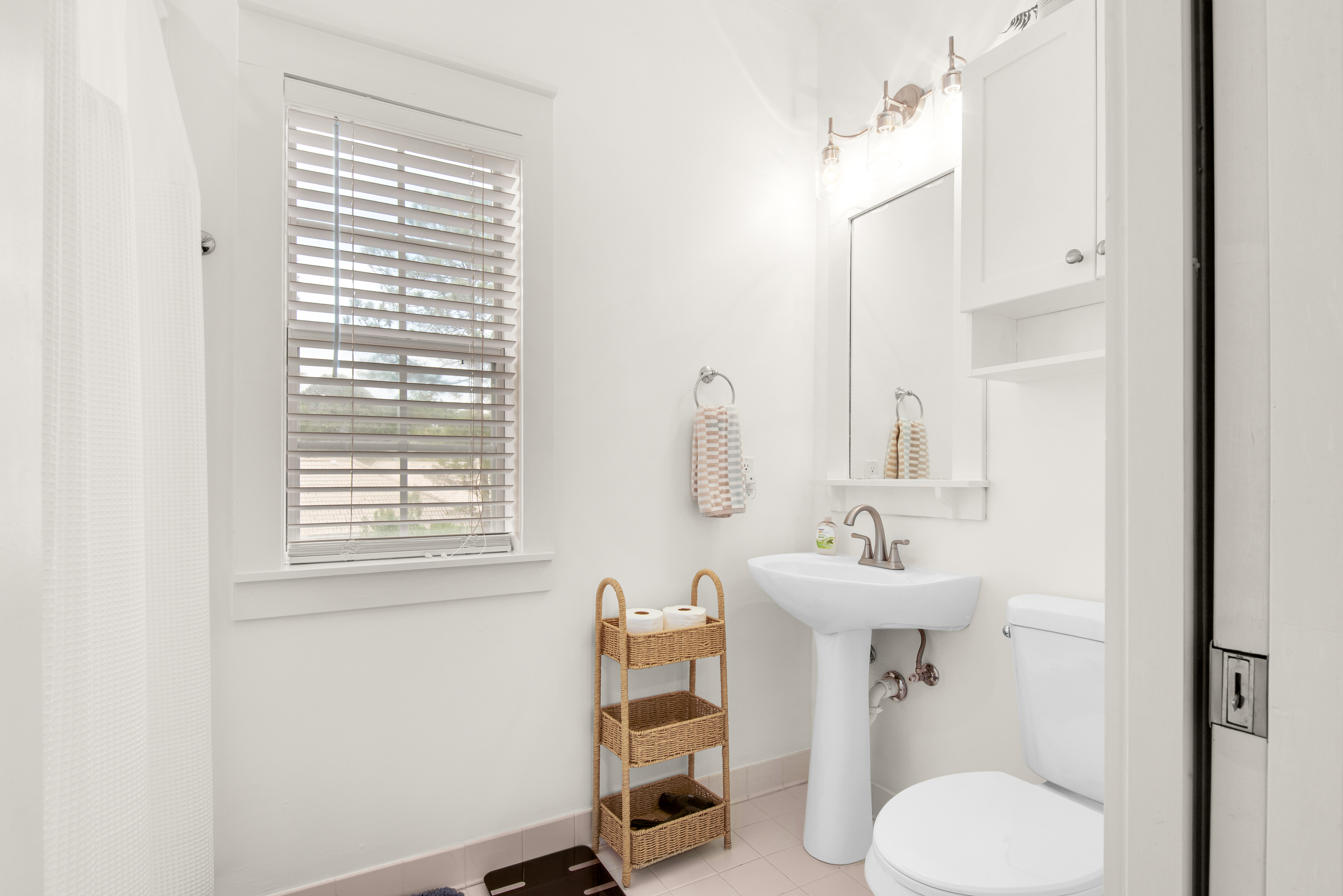 Seagrove Bungalow 103 bathroom with a pedestal sink, mirror and built-in shelving.