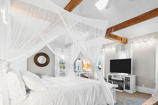 Primary suite with a king canopy bed, exposed beams, and a lighted window cupola overhead.