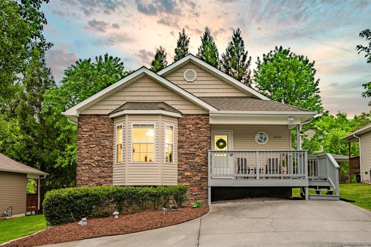 Inviting cottage-style home with stone accents, a welcoming front porch, and lush greenery—perfect for a cozy getaway in a peaceful setting.