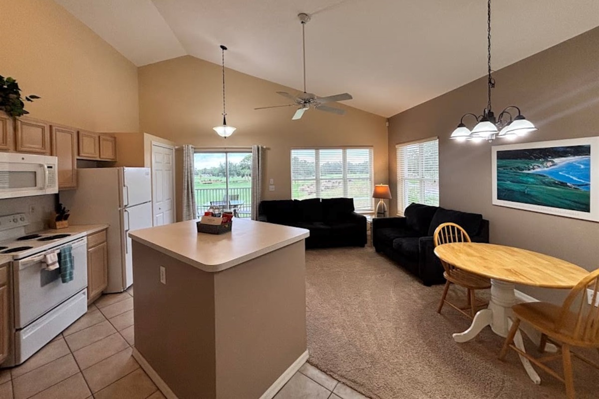 Open-concept kitchen, dining, and living area with vaulted ceilings, comfortable seating, and views out toward the screened balcony.