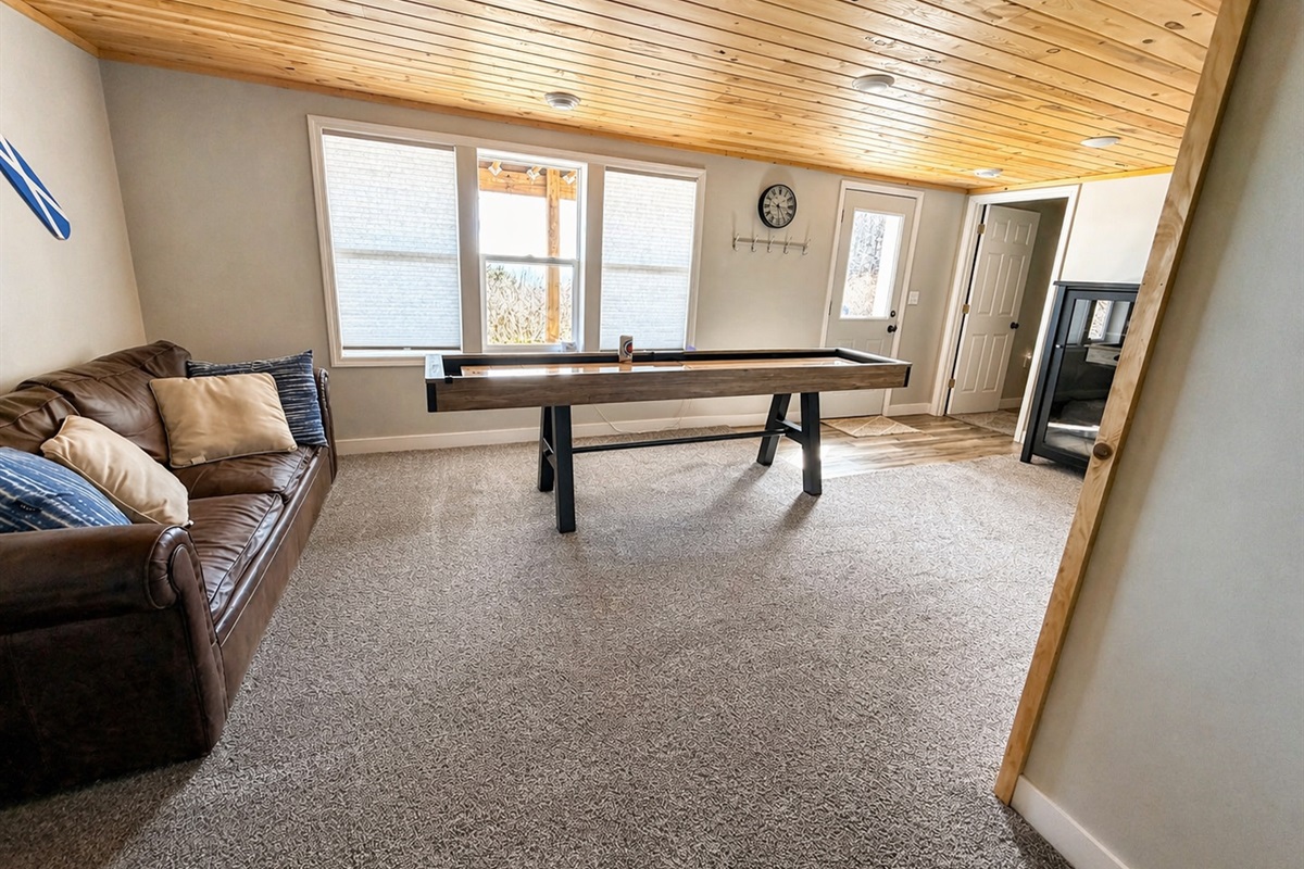 As you head back through the basement, passing the shuffleboard, large windows offer a view of the backyard, guiding you toward the bedroom. The walkout door and natural light make this space feel connected to the outdoors.