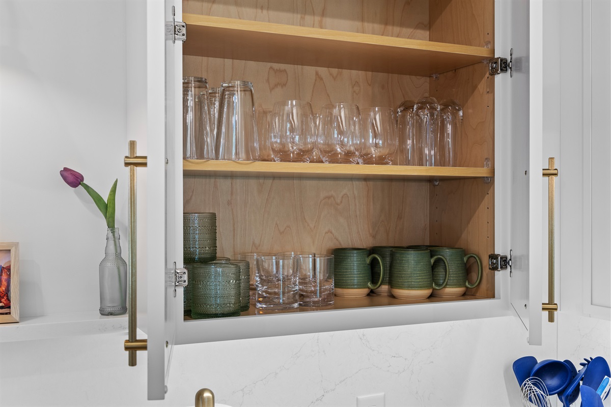 Fully stocked kitchen cabinets with glassware and mugs.
