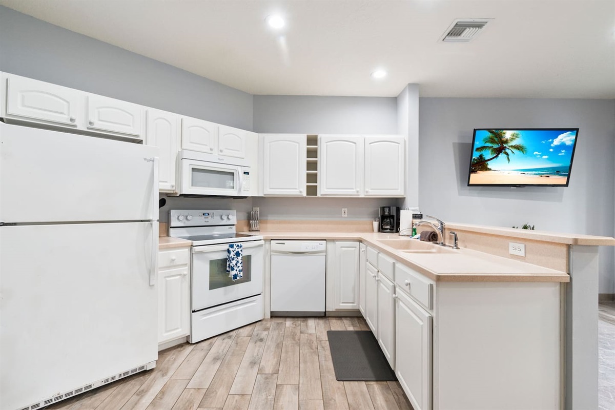 Bright kitchen with white cabinetry, full-size appliances, breakfast bar, and an open layout connecting to the living area.