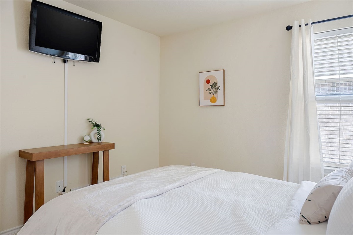 This spacious bedroom features a plush bed, a large window with natural light, and a modern TV mounted on the wall, creating a cozy retreat.