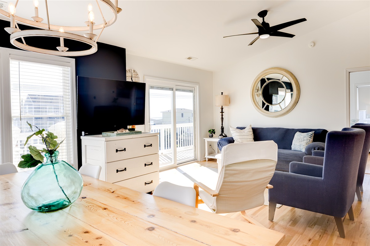 Open-concept living & dining area with a large smart TV, ceiling fan, comfy seating, and sliding doors to the private balcony