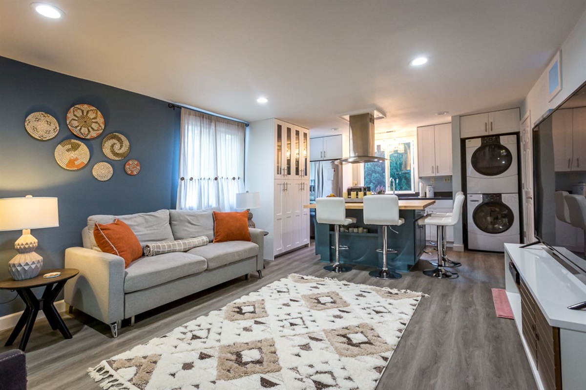 - Stylish open living area with blue accent wall and cozy gray sofa seating  
- Modern kitchen with breakfast bar seating for four and full appliances  
- Includes in unit washer and dryer for guest convenience during stays  
