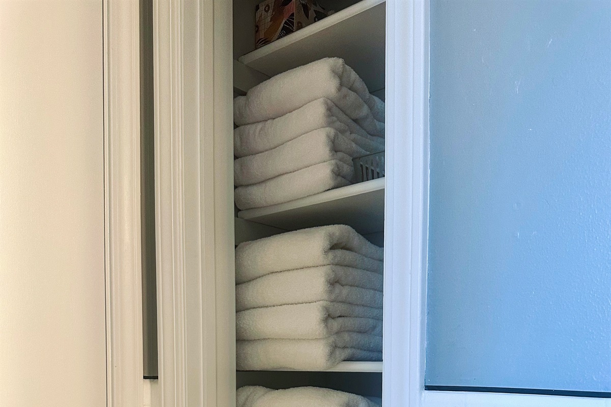 Main bathroom linen closet stocked with plush bath towels. Additional shelves (shown in alternate photos) also include hand towels, washcloths, and makeup remover cloths—everything needed for daily routines and longer-term comfort.