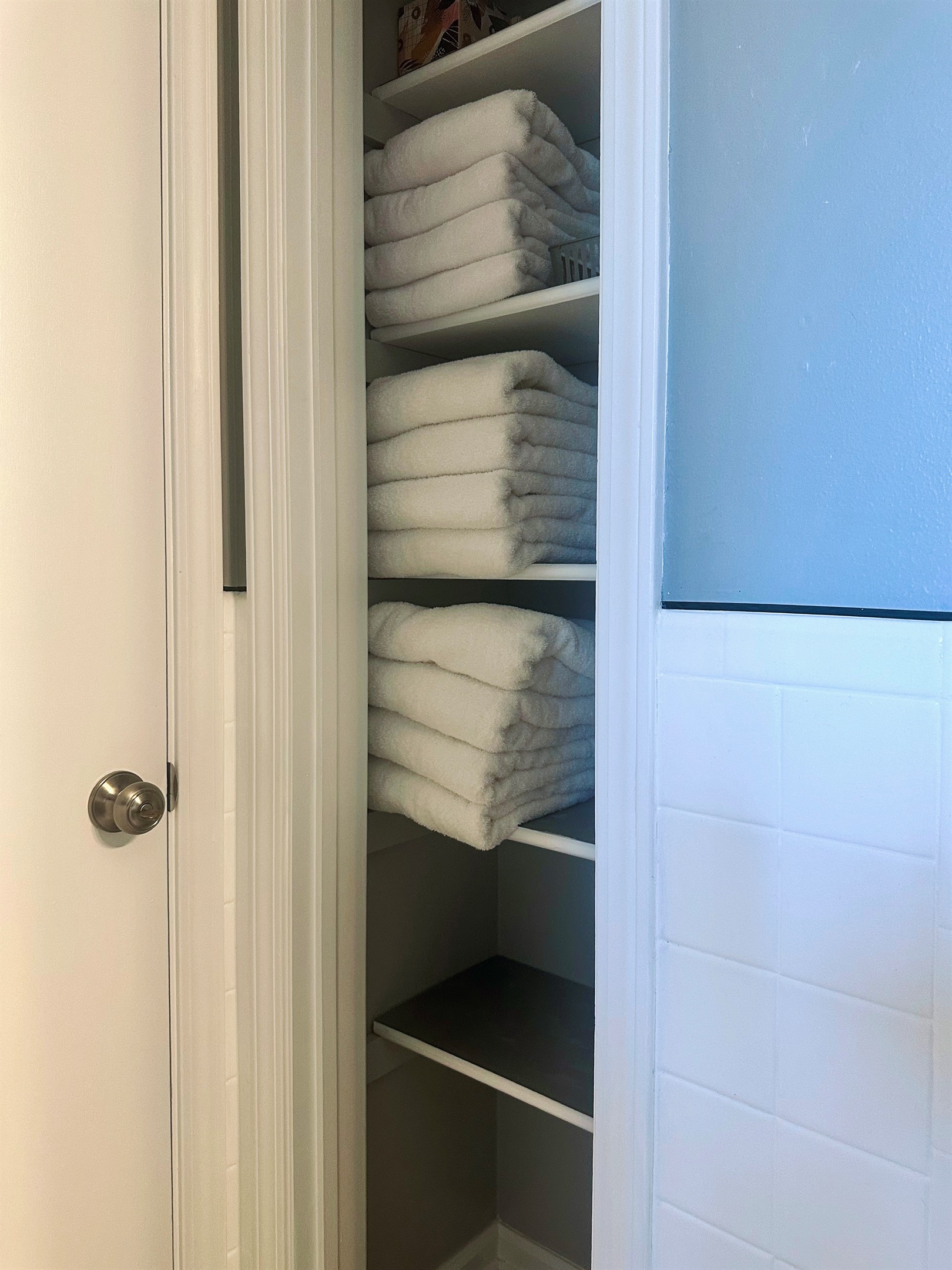 Main bathroom linen closet stocked with plush bath towels. Additional shelves (shown in alternate photos) also include hand towels, washcloths, and makeup remover cloths—everything needed for daily routines and longer-term comfort.