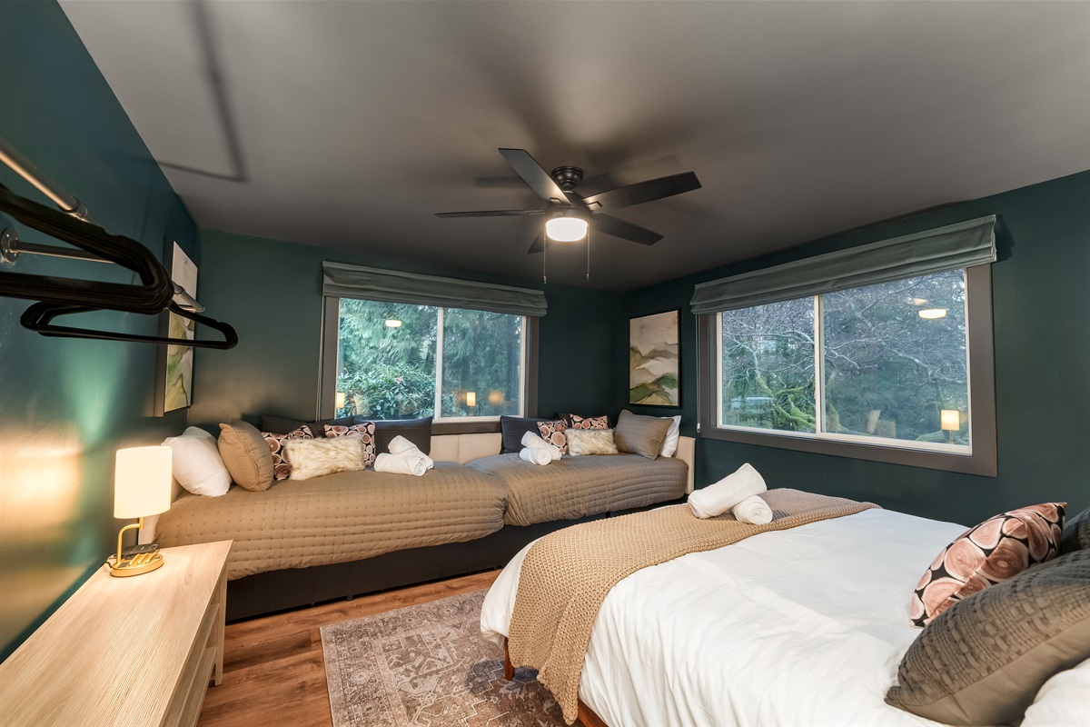 A versatile sleep space featuring a king bed and two twin beds, ideal for families or friends. Large windows frame peaceful forest scenery for a relaxing stay.