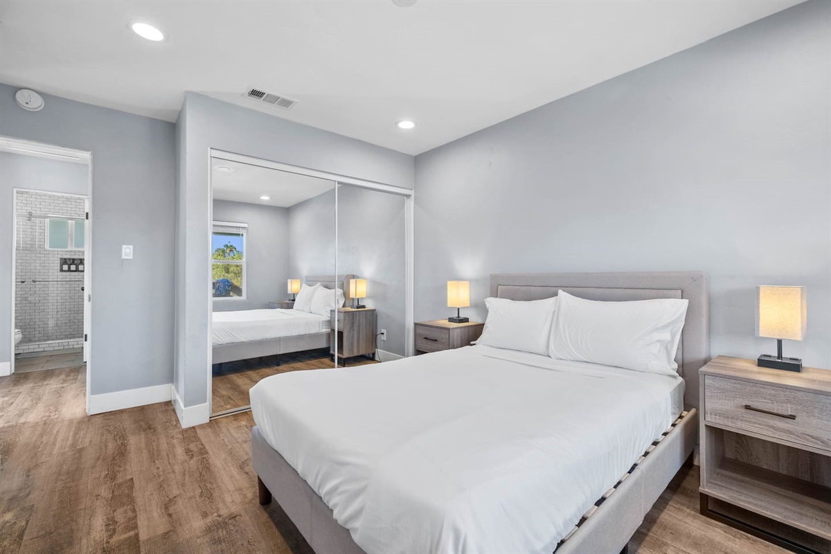 Cozy bedroom featuring a comfortable bed with two lampshades providing aesthetic lighting, a full-body mirror, and a convenient clothing container inside. A perfect blend of style and functionality for a relaxing and organized stay.
