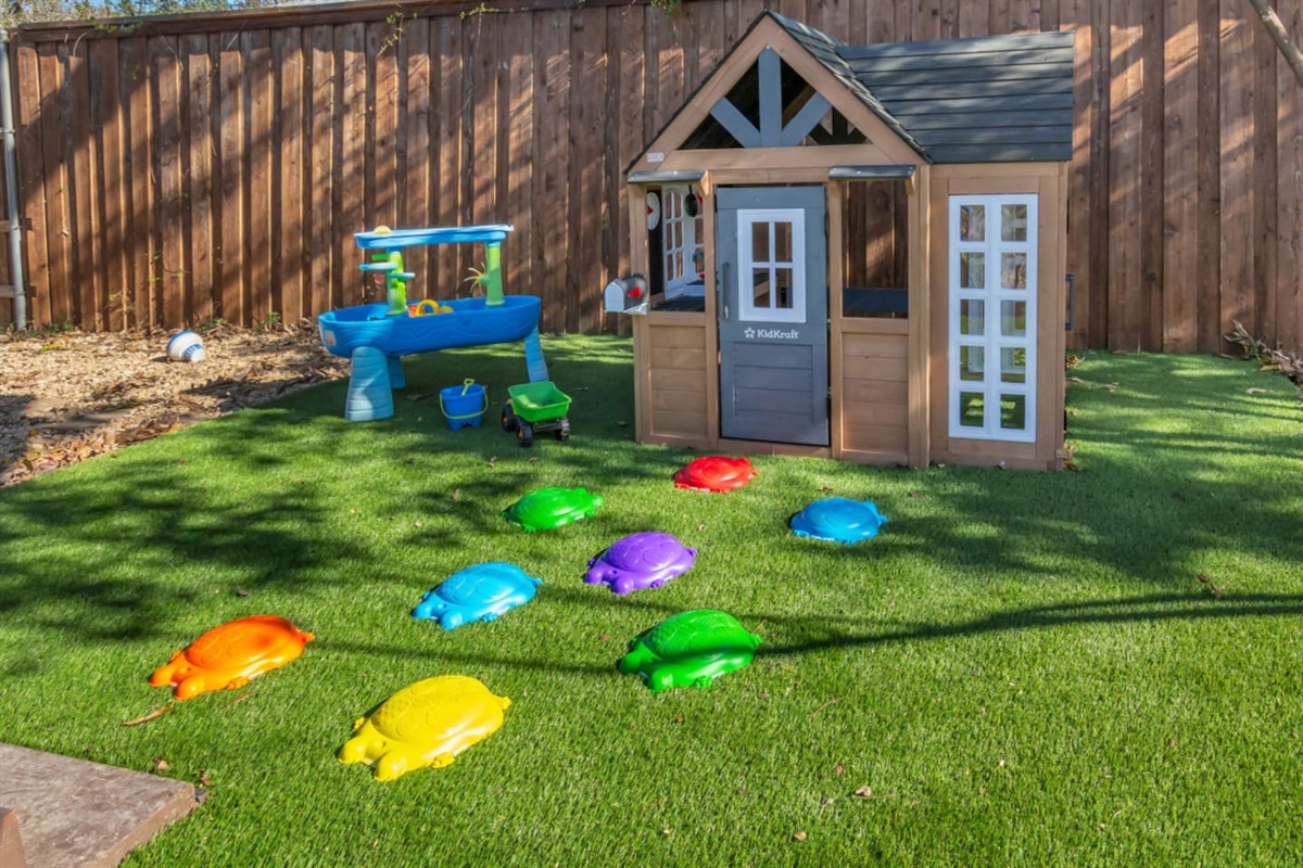 A charming backyard play zone featuring a KidKraft playhouse and colorful stepping turtles—perfect for little ones to explore, imagine, and stay entertained during your stay.