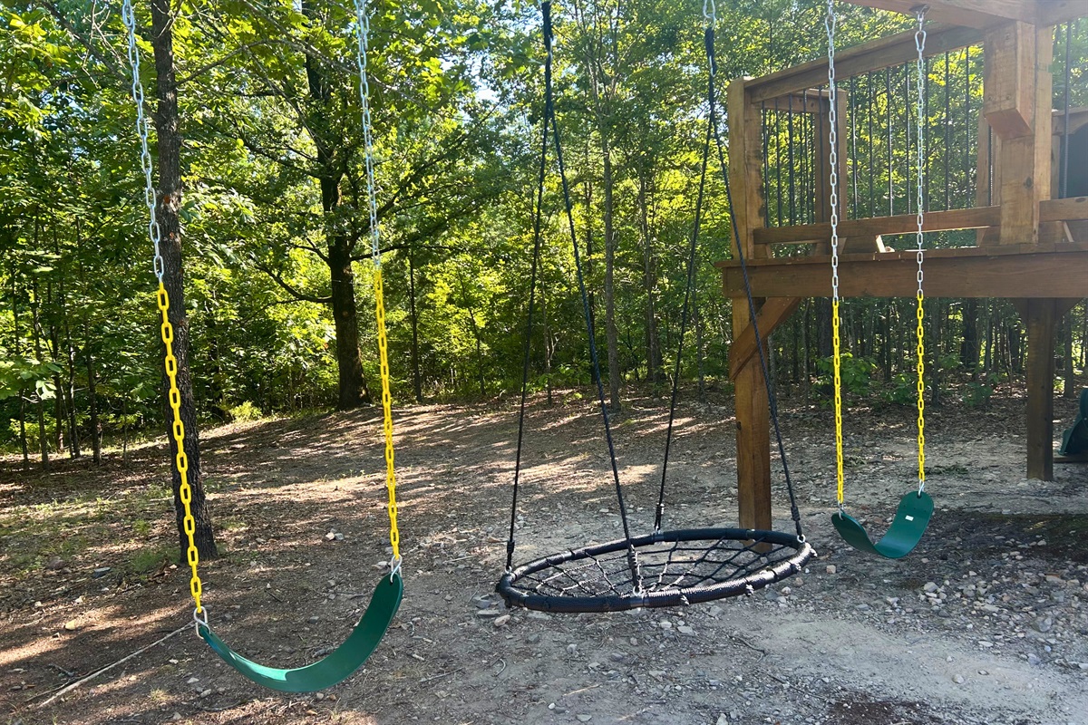 Shaded swing area with saucer, classic swings, and a forest backdrop.