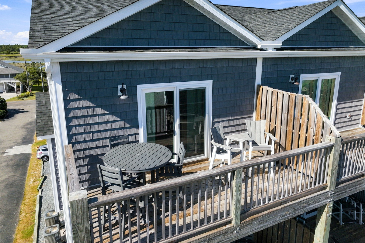 Top-floor private deck area featuring outdoor dining table seating, additional lounge chairs, sliding door access, and a wooden privacy divider.   
