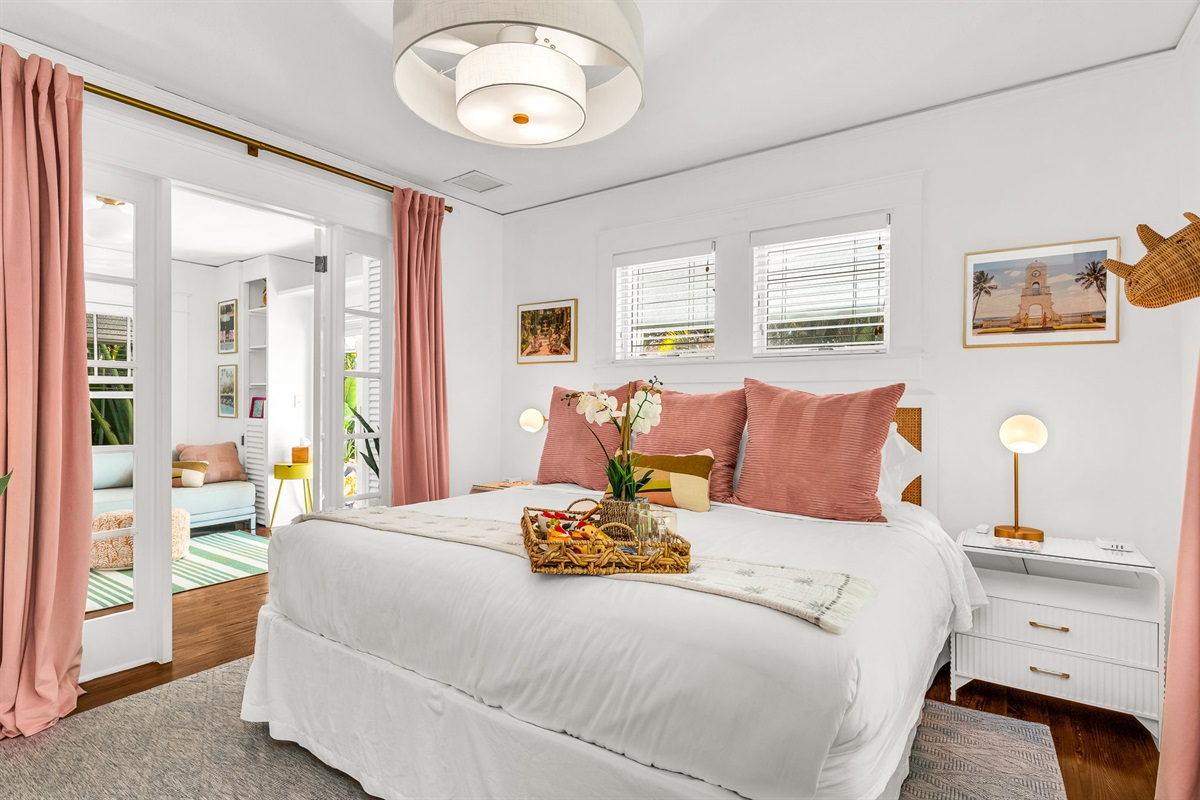 Primary bedroom with a king bed, smart TV, and ensuite bath featuring an antique soaking tub and modern shower. Cane rattan headboard, blackout drapes, and Palm Beach art add charm. Opens to the 4th bedroom, ideal for a private family suite.