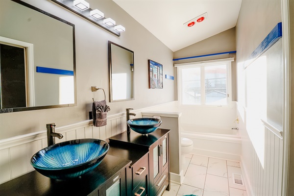 A bathroom featuring a unique blue sink, a wide mirror for an expansive feel, and a comfortable bathtub, blending functionality with serene aesthetics.