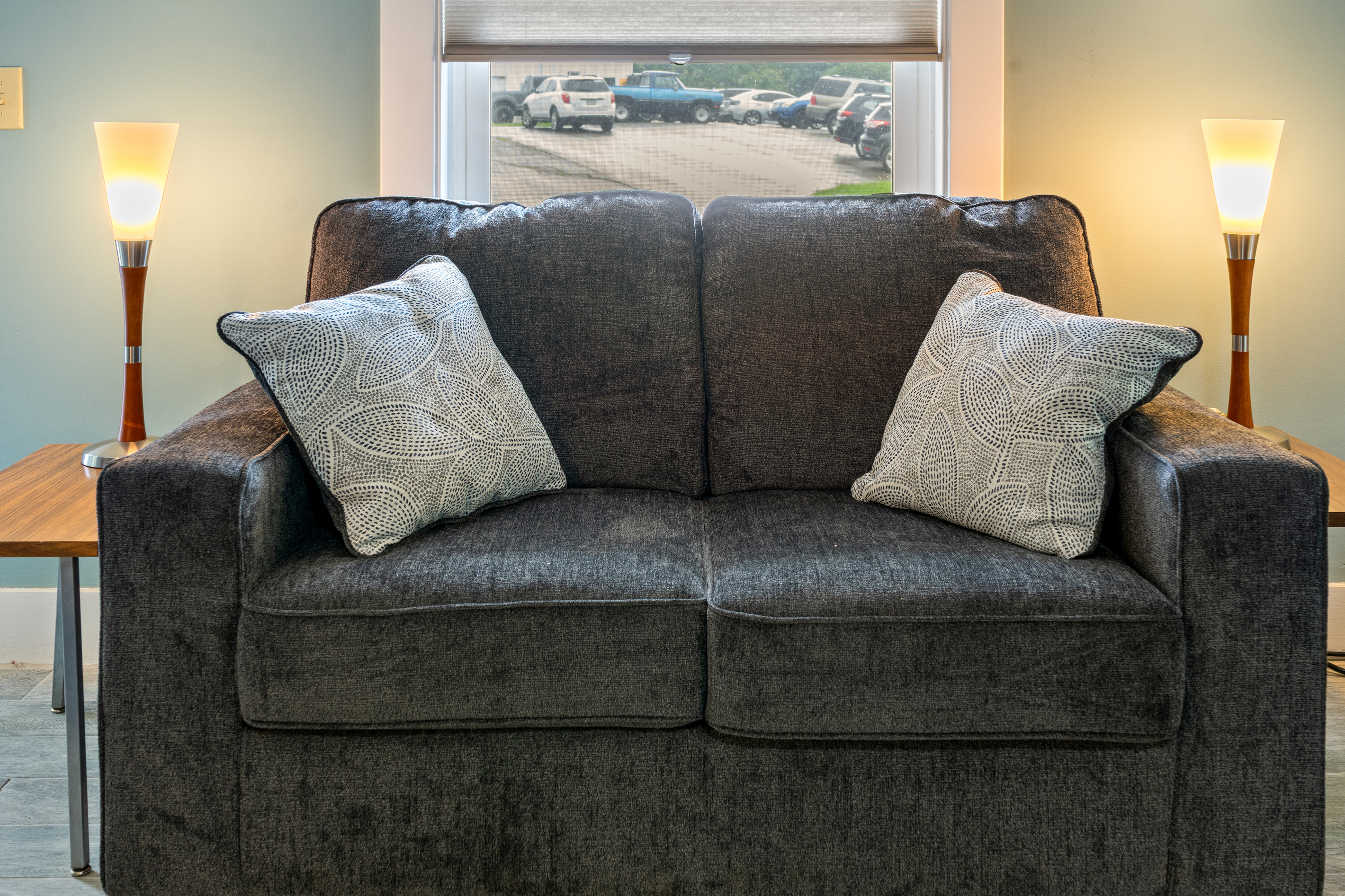 This closer perspective shows the deep cushions of the plush loveseat, flanked by warm reading lamps. Whether you are scrolling through photos from Acadia or chatting with family, this balanced setup offers a comfortable spot for group downtime.