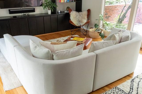 The curved sectional wraps around the TV for movie nights, with warm wood paneling and plants keeping the whole room easy and inviting.