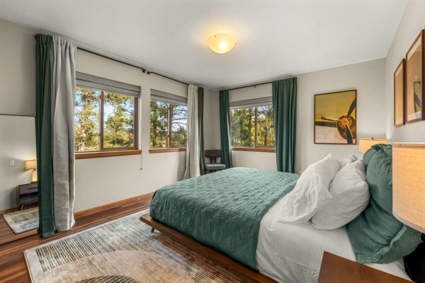 🛏️🌲 Bright, airy main-level bedroom with corner windows, crisp linens, and calming forest views ✨—perfect for slow mornings and restful nights.