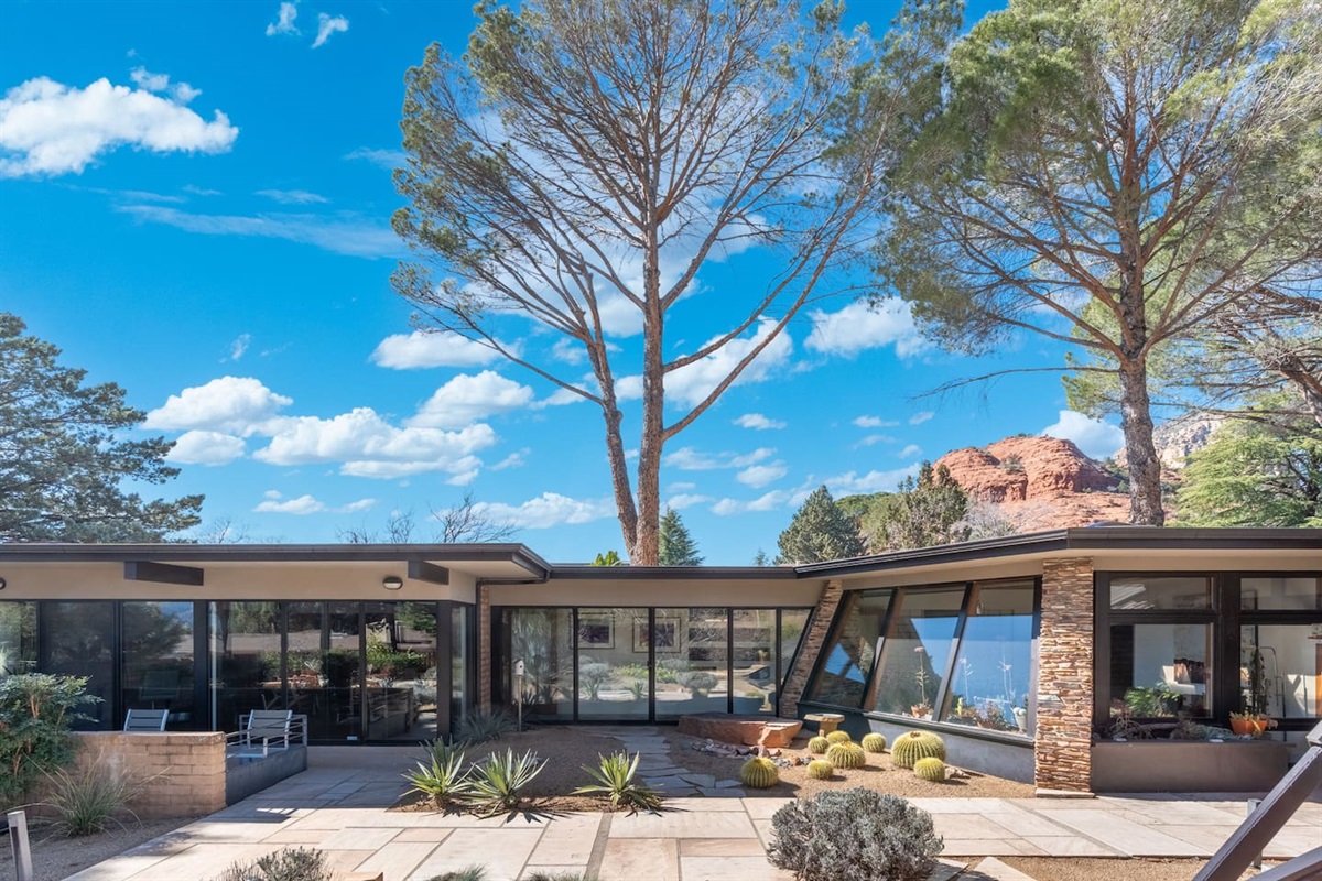 Iconic mid-century design with floor-to-ceiling glass, desert landscaping, and Sedona’s red rocks rising just beyond.