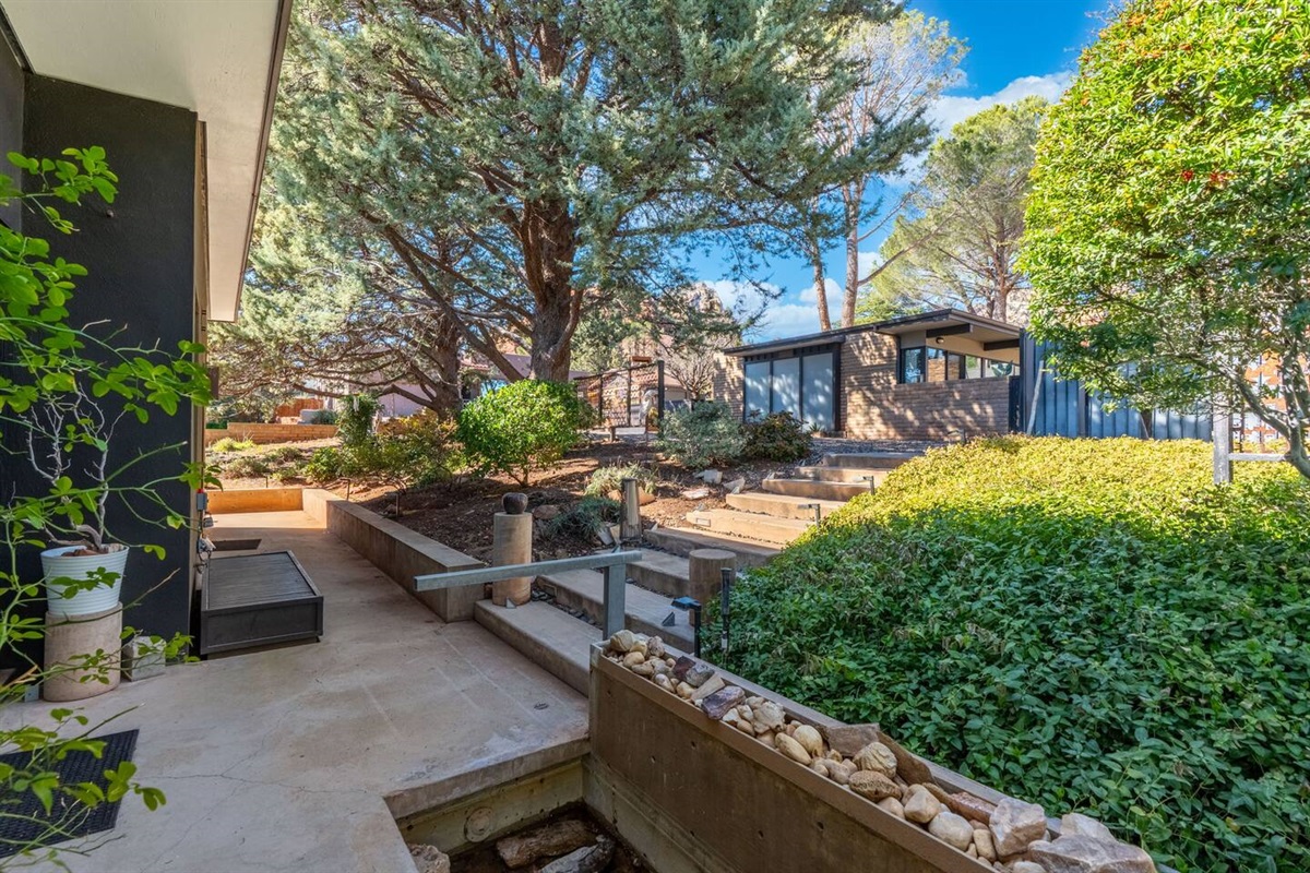 Peaceful landscaped courtyard with mature trees, stone steps, and modern mid-century architecture.