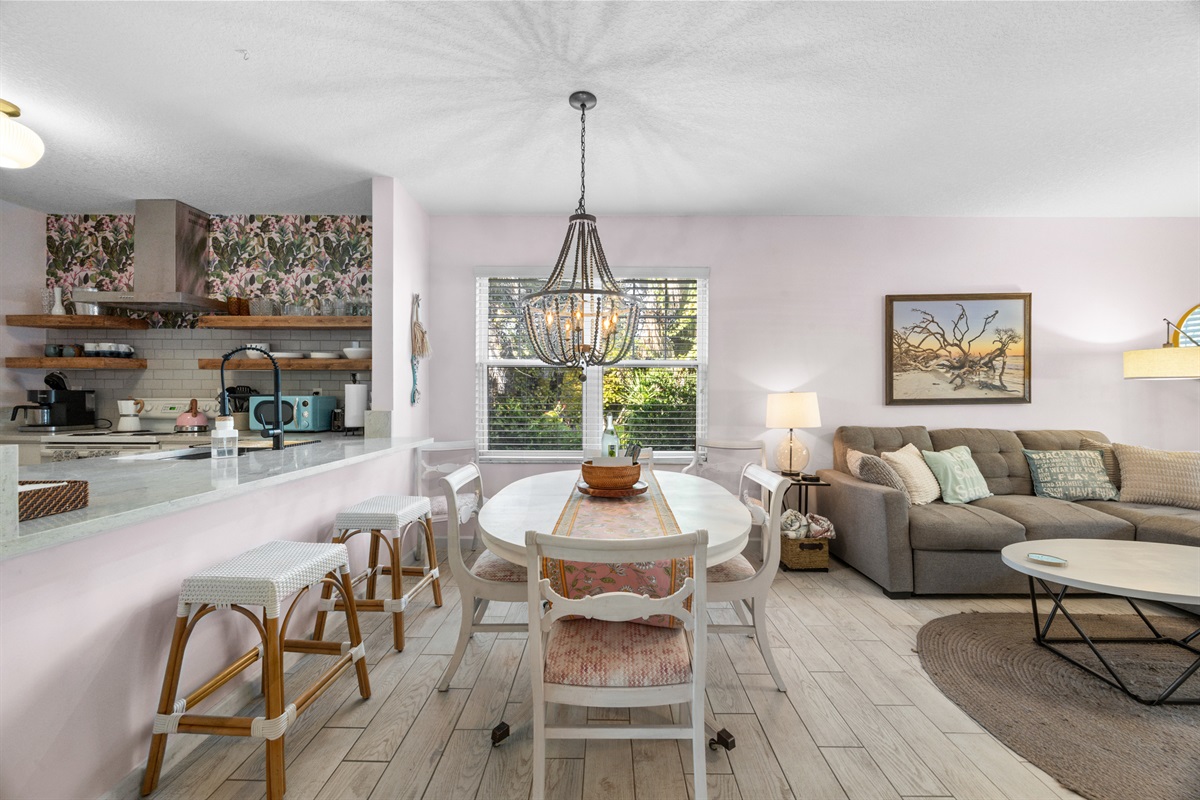 Charming dining space with elegant chandelier, seating for six (and extenders for more), open kitchen with bar for seating, and warm natural light.