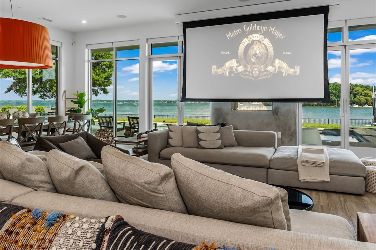 Living room with walls of glass with 120" projector screen down during daylight.