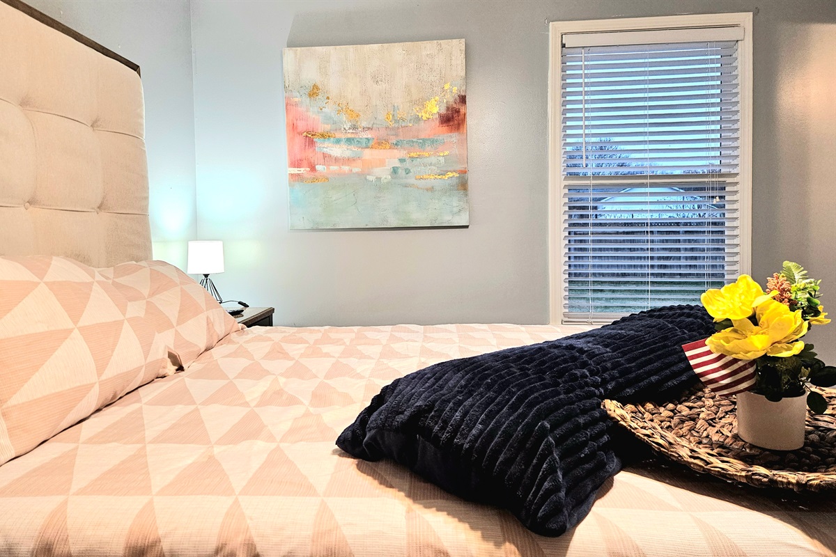 Queen primary bedroom with extra seating, ceiling fan, fast WIFI, TV, ensuite bathroom, and walk-in closet. Big window overlooking the fenced back yard adds fresh natural light and appeal.