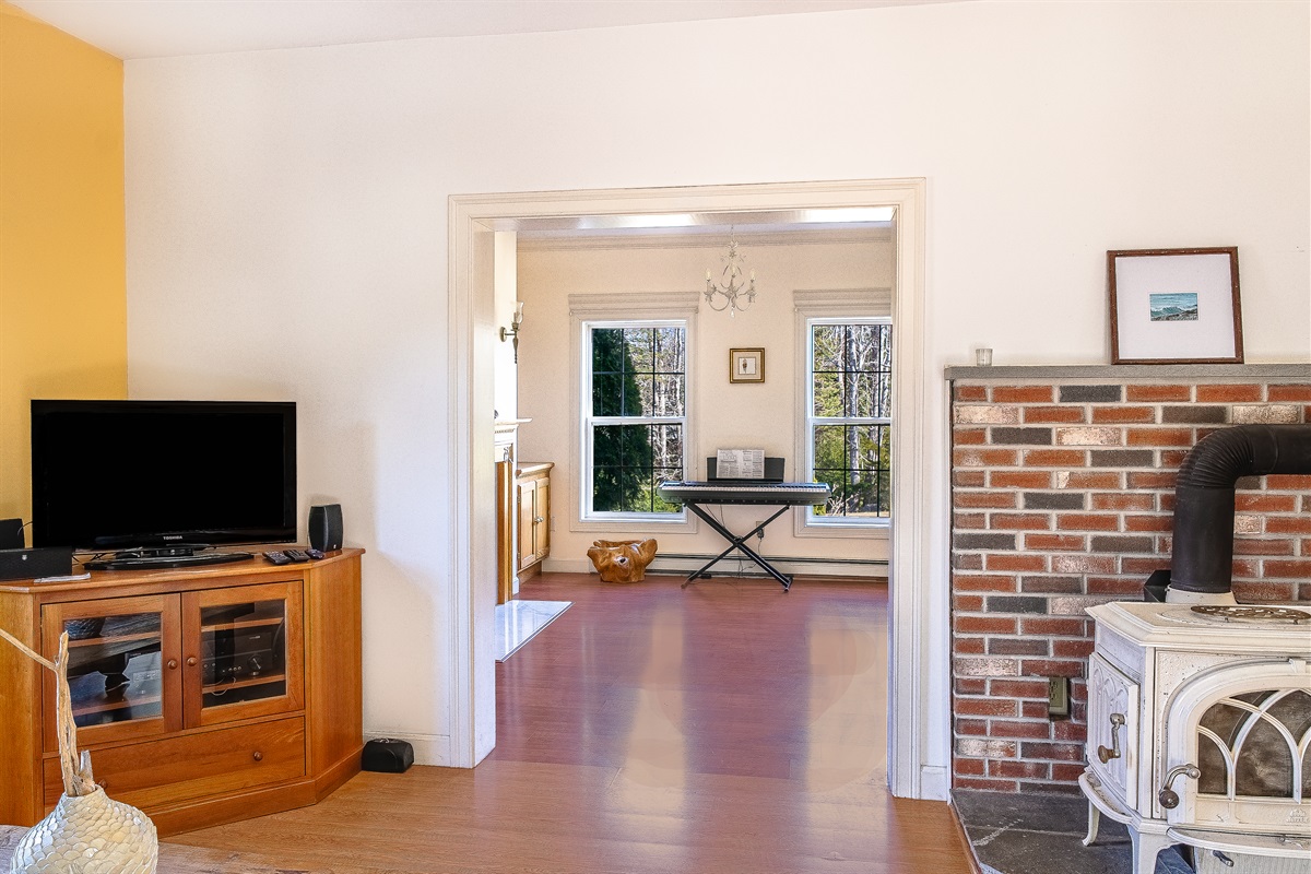 Step from the living room into the Driftwood Den, a charming, multi-use space. Note the brick hearth with its white, decorative-only wood stove. Guests are welcome to play the electric keyboard—a unique feature for musicians in Southwest Harbor.