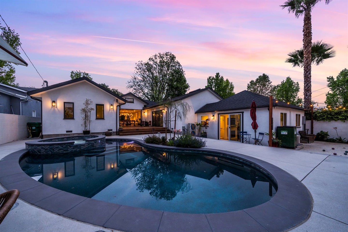 The peaceful beauty of the backyard, blending the soft glow of the houses with the shimmering pool.