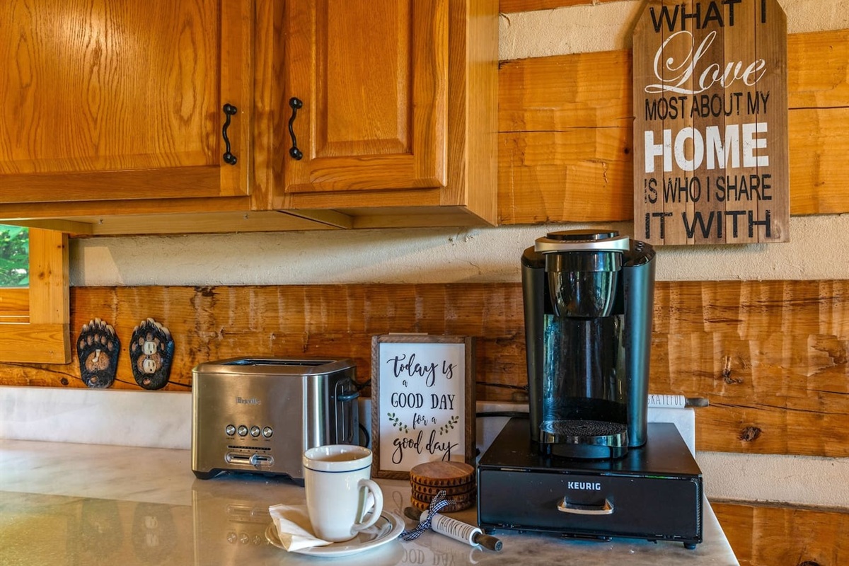 Cozy Kitchen corner with the coffee station. A toaster, Keurig coffee maker, and "Today is a Good Day" sign add to the warm vibe. View of greenery outside.