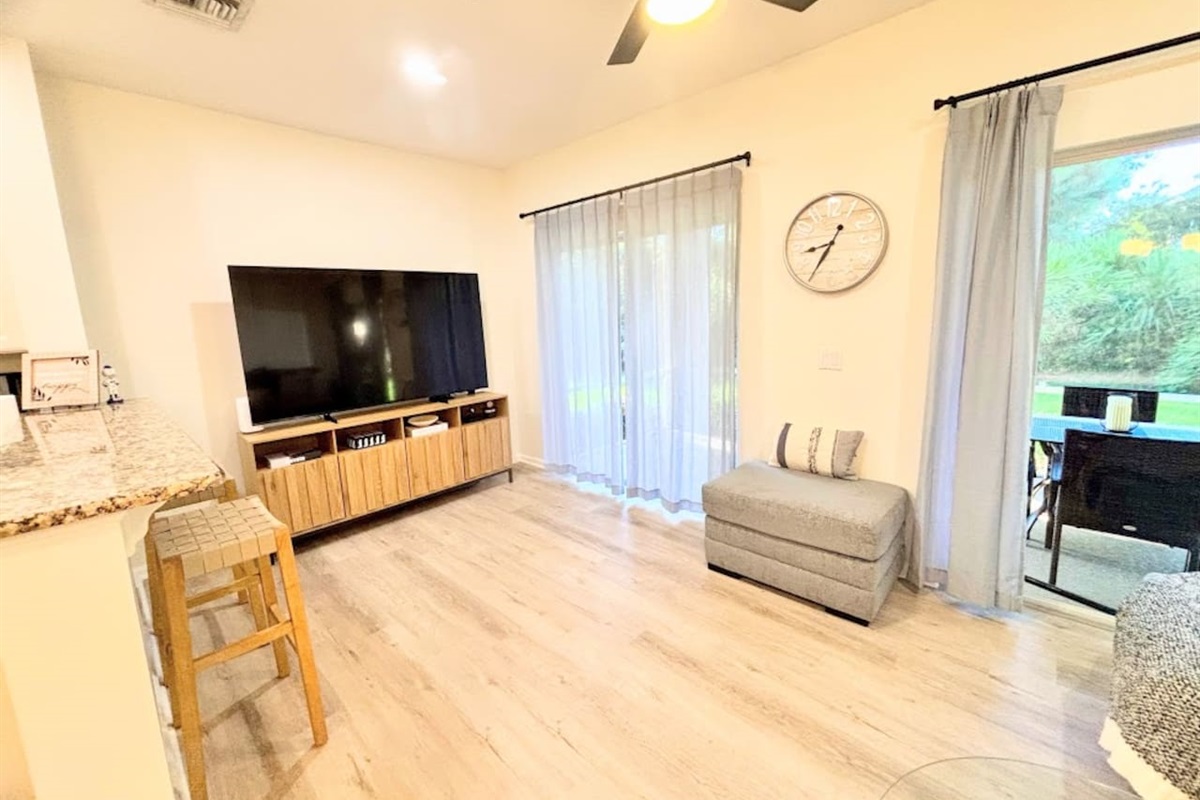Modern living area with wood-look flooring, large TV, stylish decor, and sliding glass doors that open to the outdoor patio space.