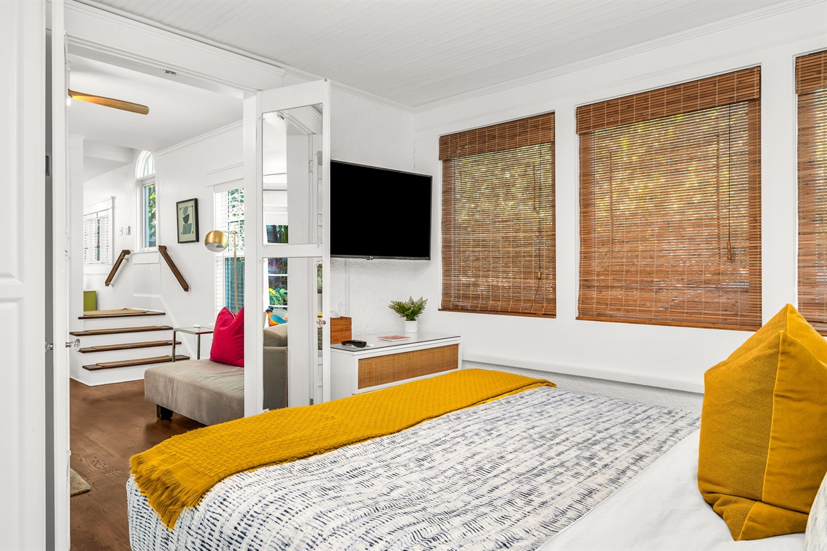 Charming first-floor queen bedroom just off the main living area, featuring a queen bed, a smart TV, bamboo shades, and French doors that fill the room with natural light.