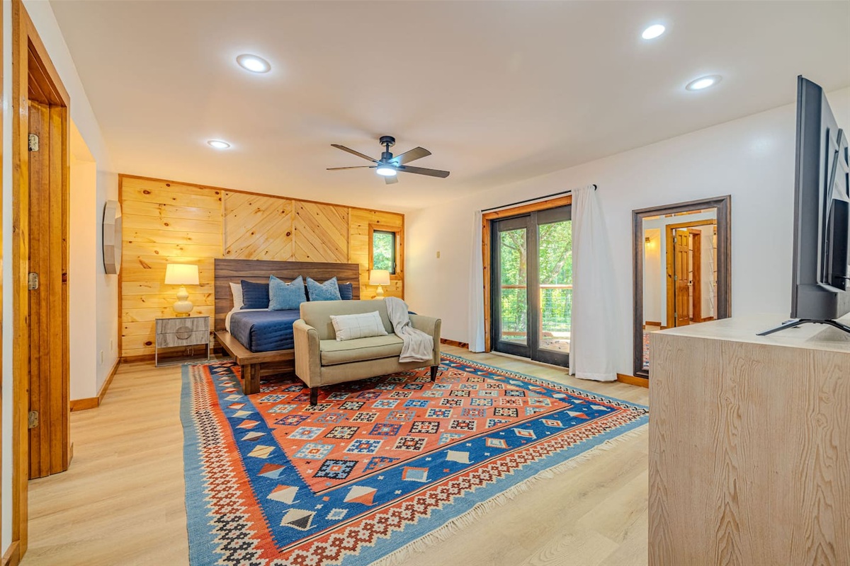 Retreat to the spacious primary suite on the main floor, where a striking wood accent wall frames the king bed and soft natural light pours in, with direct access to the back deck for peaceful mornings.
