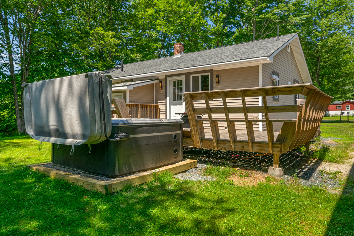Step from the grass lawn directly onto the outdoor deck entertainment space. View showcases the dedicated timber base supporting the private 6-person hot tub, the integrated wooden bench seating, and the rear entry door into the main home.