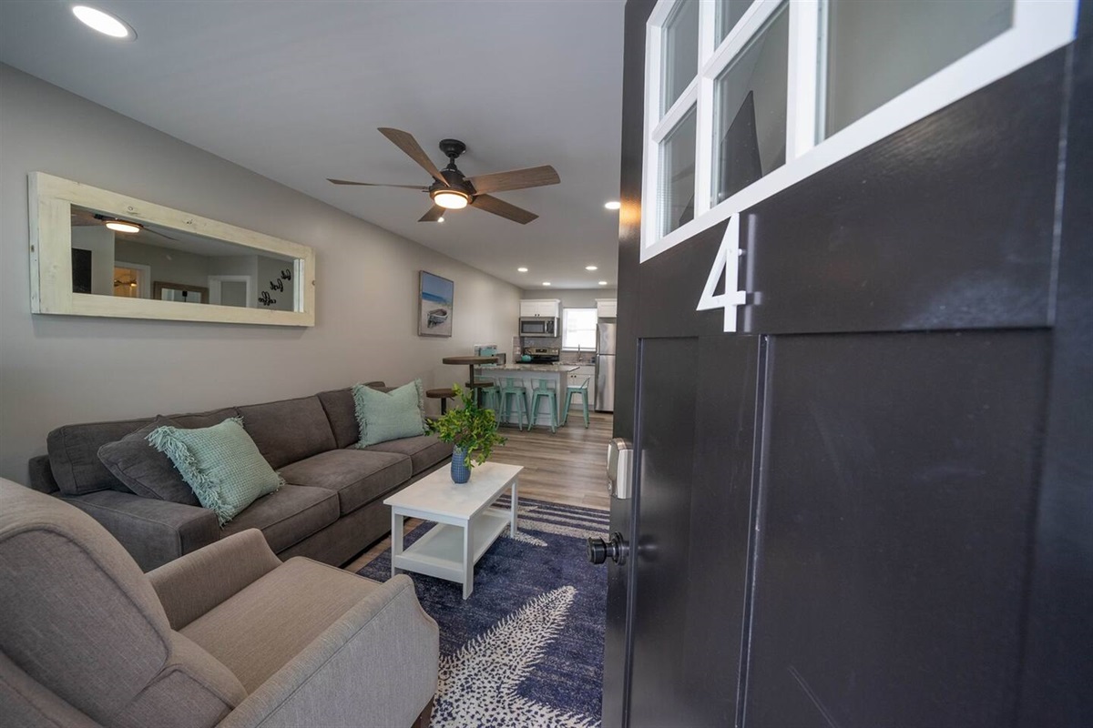 Step inside to a bright, open living space with comfortable seating, soft coastal tones, and warm lighting. The layout flows seamlessly from the lounge to the kitchen, creating an inviting area to relax, unwind, and settle in after arrival.