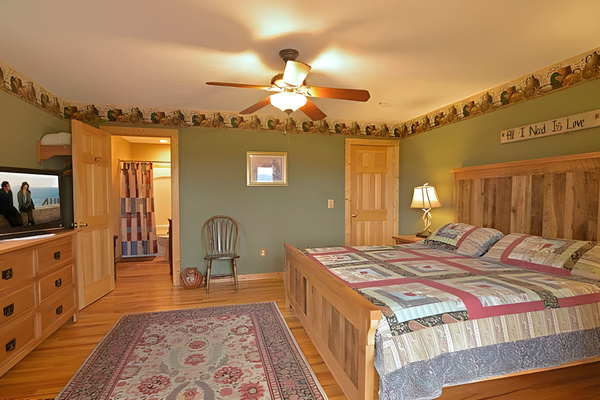 Conveniently located right off the main living area, the space features a comfortable king-size bed with a rustic wooden headboard, a flat-screen TV, and its own private en-suite bathroom.